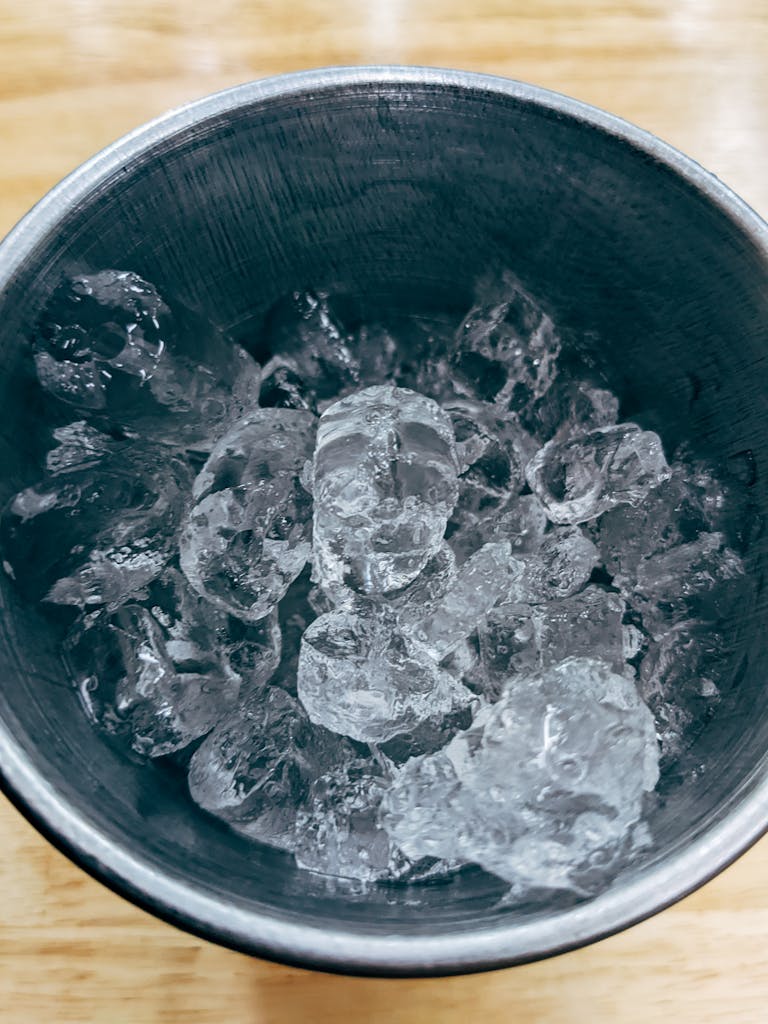 Detailed overhead view of crystalline ice cubes in a metal bucket on wooden surface.