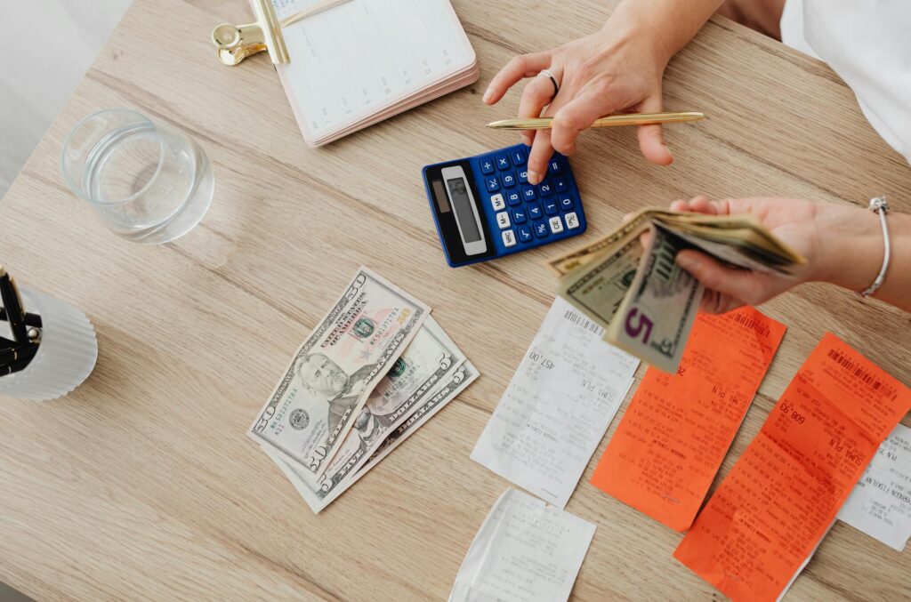 Overhead view of a person using a calculator to manage cash and receipts at a desk.